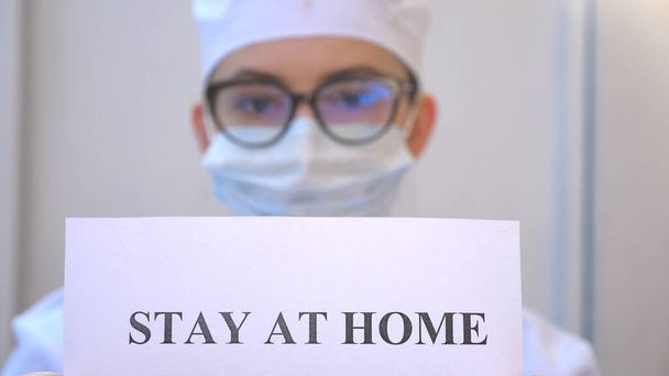 Női orvos tart egy képet a felirat marad otthon a koronavírus járvány alatt. A mentősök azt mutatják, hogy a plakát az elszigeteltségre utal. A biztonsági élettartam koncepciója a COVID-19 világjárványból. - Fotó, kép