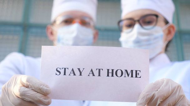 Mies- ja naislääkäreillä on kuva, johon on kaiverrettu kotona sepelvaltimotautiepidemian aikana. Lääkintämiehet esittelevät julisteen, jossa vedotaan eristäytymiseen ja turvallisuuteen COVID-19-pandemiasta. - Valokuva, kuva