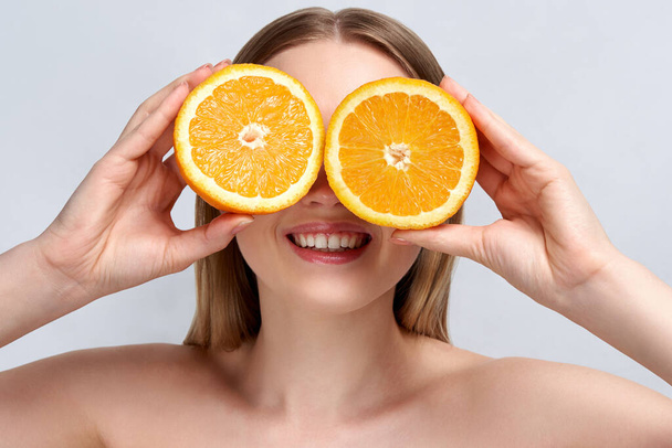 Pretty charming joyful attractive cheerful funny comic positive nude natural pure girl having two pieces of orange, on blue background. isolated on beige background with copy space for advertisement. Skincare. Vitamin C. Blonde woman - Фото, зображення