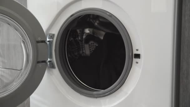 Női kéz, házas gyűrűvel, fehér ruhákat vesz ki a mosógépből. Mosógép betöltése. Ruhákat a mosógépbe. Ruha mosógép betöltése. Mosás előkészítése - Felvétel, videó