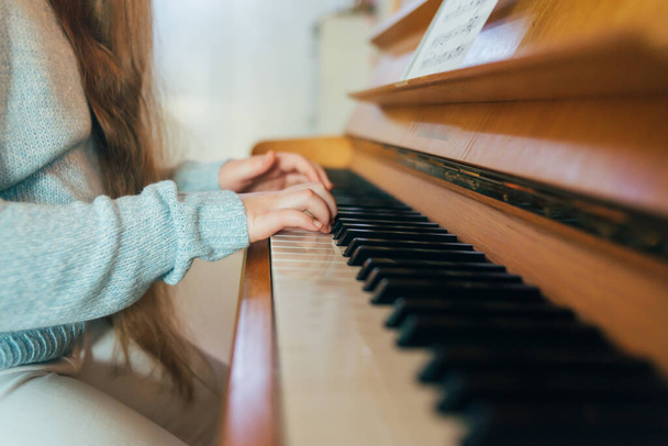 Девочка практикует уроки фортепиано дома. Крупный план детских рук, играющих на пианино, музыкальные ноты на коричневом пианино
 - Фото, изображение