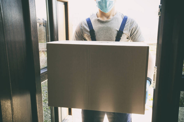 The courier is delivering the carton box to the home  wearing latex gloves and medical mask - Fotografie, Obrázek