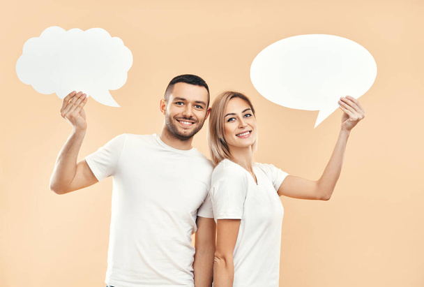 Smiling woman and man holding paper thought bubbles over beige background. relationship concept - Foto, immagini