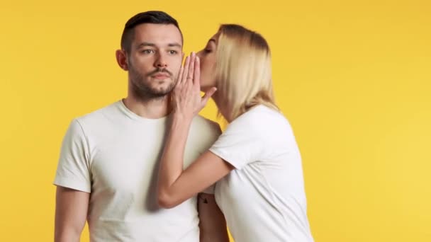 woman whispering something to her boyfriend on yellow background - Filmati, video