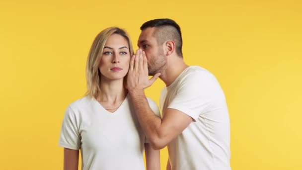 man whispering something to his girlfriend on yellow background - Video