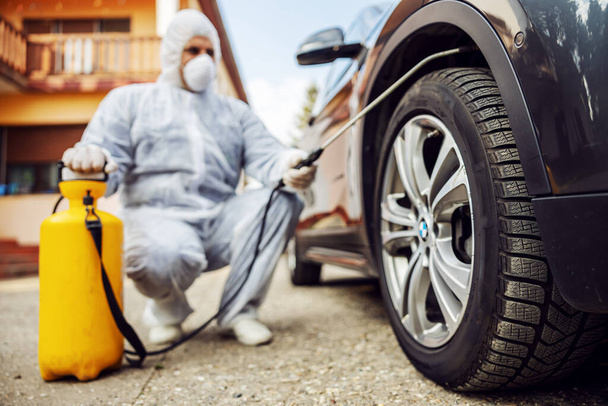 Man in protective suit with mask disinfecting car tires, prevent infection of Covid-19 virus coronavirus,contamination of germs or bacteria. Infection prevention and control of  - Photo, Image