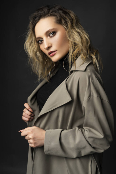 Beautiful girl wearing a casual trendy trousers, turtleneck and raincoat posing on a dark background. Fashionable, advertising, lifestyle and commercial design - Φωτογραφία, εικόνα