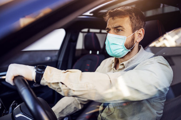 Άντρας με προστατευτική μάσκα και γάντια που οδηγεί αυτοκίνητο. Πρόληψη λοιμώξεων και έλεγχος επιδημιών. Παγκόσμια πανδημία. Να προσέχεις.. - Φωτογραφία, εικόνα