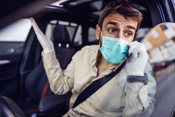 Man with protective mask and gloves driving a car talking on mobile phone smartphone. Infection prevention and control of epidemic. World pandemic. Stay safe. - Photo, Image