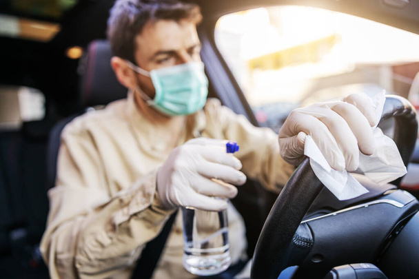 Άνδρας με προστατευτική στολή με μάσκα απολυμαίνει το εσωτερικό του αυτοκινήτου, Άνδρας με προστατευτική στολή με μάσκα απολυμαίνει το εσωτερικό του αυτοκινήτου, σκουπίζει καθαρές επιφάνειες που αγγίζονται συχνά, προλαμβάνει τη μόλυνση του ιού Covid-19 coronavirus, μόλυνση των μικροβίων ή βακτηρίων. Ι - Φωτογραφία, εικόνα