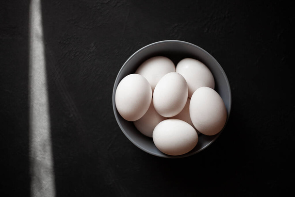 Plate filled with eggs.More than four eggs.Photo taken on concrete background.Gray plate and chicken eggs.The sun's rays fall into the frame. - Photo, Image