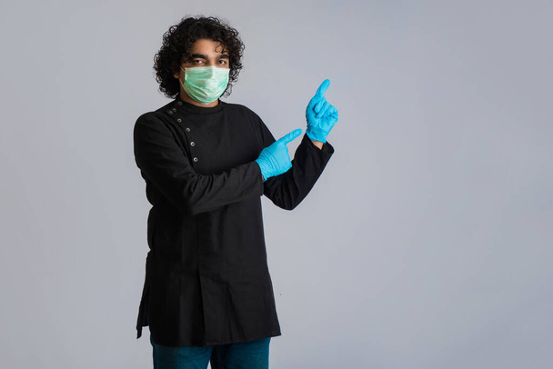 Jeune homme portant un masque médical montrant quelque chose sous la main. un homme portant un masque chirurgical pour se protéger du coronavirus
. - Photo, image