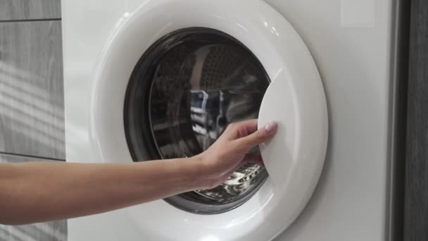 La mano femenina con anillo de casado pone ROPA GRIS en la lavadora. Cargando lavadora. Carga la ropa a la lavadora. Carga la ropa lavadora. Preparación del lavado de ropa
 - Imágenes, Vídeo