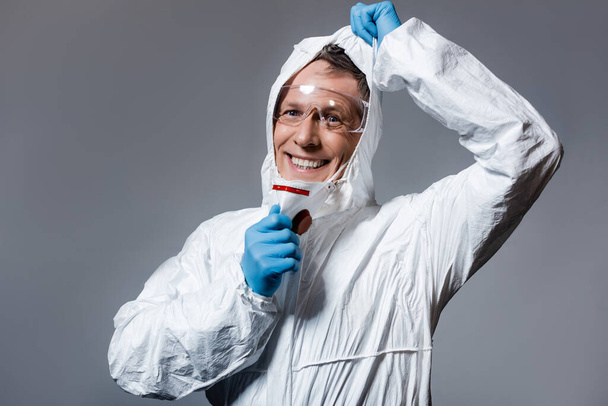 cheerful and mature man in hazmat suit and goggles isolated on grey  - Фото, изображение