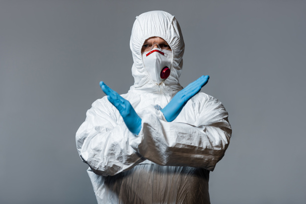 médico maduro en traje de materiales peligrosos, máscara médica y guantes de látex de pie con los brazos cruzados aislados en gris
  - Foto, Imagen