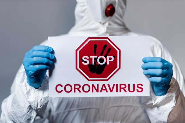 vista ritagliata del medico maturo in tuta hazmat tenere cartello con arresto coronavirus lettering isolato su grigio
 - Foto, immagini