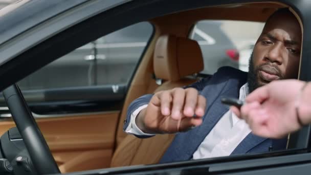 車の前に座っているアフリカ人の男を閉じます。ビジネスマンが車の鍵を取って - 映像、動画