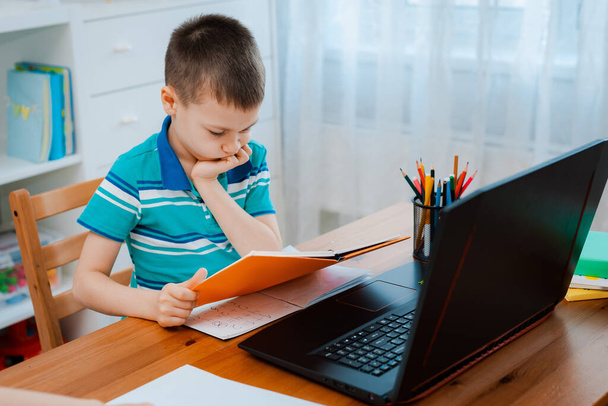 Enseignement à distance en ligne. Un écolier étudie à la maison et fait ses devoirs à l'école. Un enseignement à distance à domicile. - Photo, image