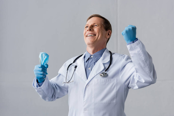 médico alegre y maduro en guantes de látex con máscara médica en gris
 - Foto, Imagen
