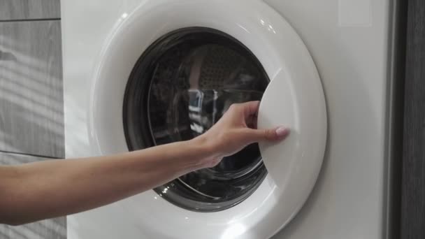 A női kéz kiveszi a fekete ruhát a mosógépből. Mosógép betöltése. Ruhákat a mosógépbe. Ruha mosógép betöltése. Mosás előkészítése - Felvétel, videó