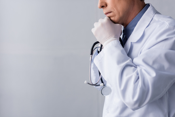 przycięty widok zamyślonego i dojrzałego lekarza w białym płaszczu na szarości - Zdjęcie, obraz