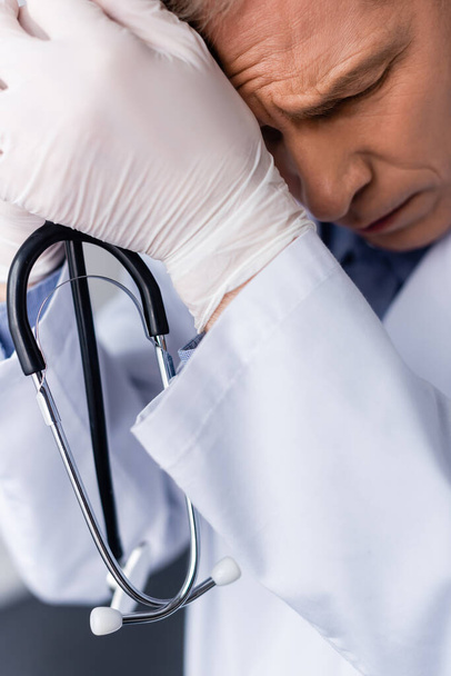 unavený a zralý lékař se zavřenýma očima držící stetoskop  - Fotografie, Obrázek