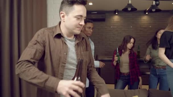 Multiracial group of young people is dancing drinking beer having fun at home party in the living room. Youth and holiday concept - Séquence, vidéo