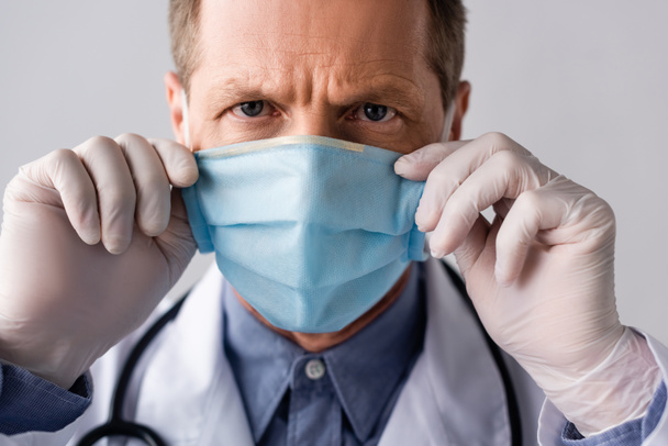 mature médecin toucher bleu masque médical isolé sur gris
  - Photo, image