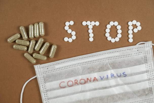 Остановить коронавирус понятие: слово СТОП написано с белыми таблетками и лекарственной защитной маской. Вид сверху
 - Фото, изображение