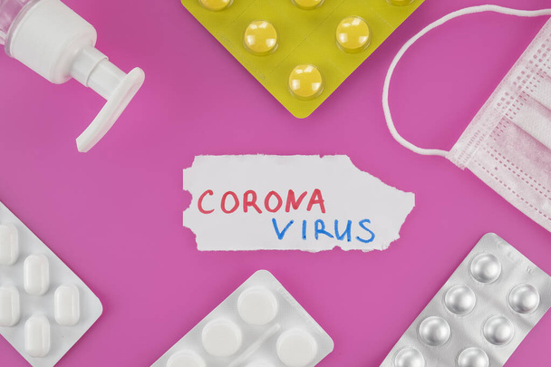 Coronavirus koncepció: pirulák, fertőtlenítők és orvosi védő maszkok rózsaszín háttér felett. Felülnézet, lapos fektetés - Fotó, kép
