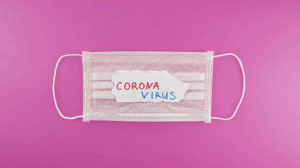 Koruyucu maske ve pembe arka planda CORONAVIRUS metni. Koronavirüsü durdurun. Üst görünüm - Fotoğraf, Görsel