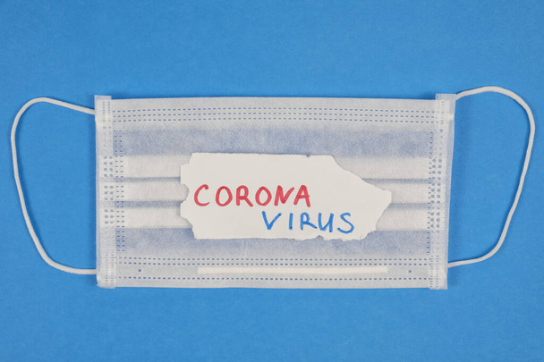 Védőmaszk és CORONAVIRUS szöveg kék háttérrel. Coronavirus háttér. Felülnézet - Fotó, kép
