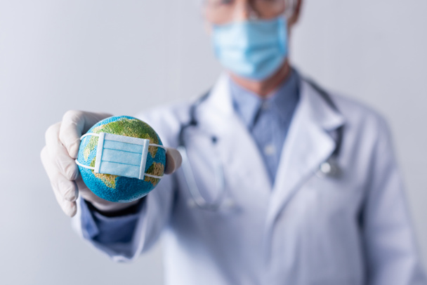 szelektív fókusz érett orvos latex kesztyű gazdaság kis földgömb orvosi maszk szürke - Fotó, kép