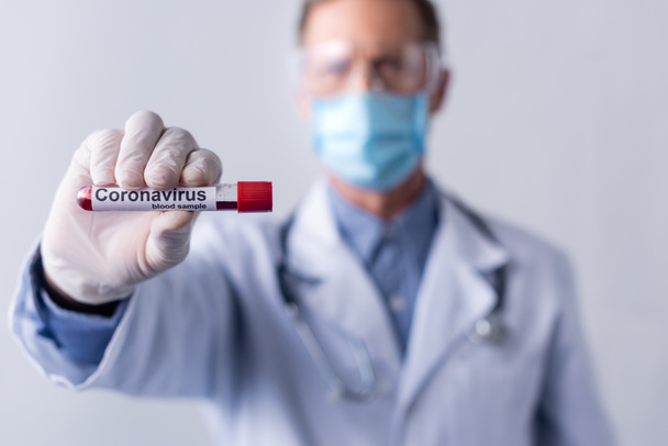 selective focus of mature doctor in medical mask holding test tube with coronavirus blood sample lettering isolated on grey - Fotografie, Obrázek