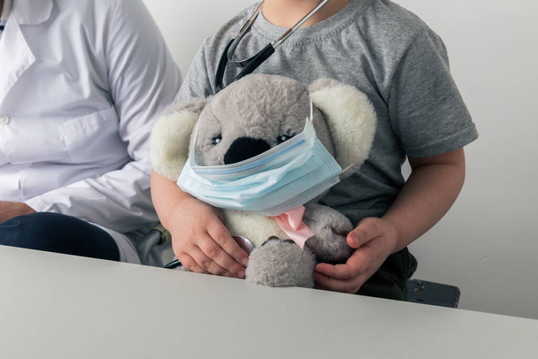 Concepto de seguridad. Hombre y niño pequeño con koala juguete en la máscara sentado en el gabinete
. - Foto, imagen