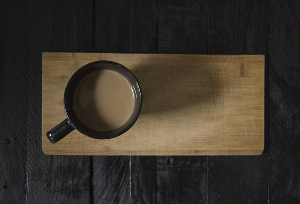 Café con leche sobre mesa de madera vista desde arriba, sobre mesa de madera negra con fondo gris
. - Foto, Imagen
