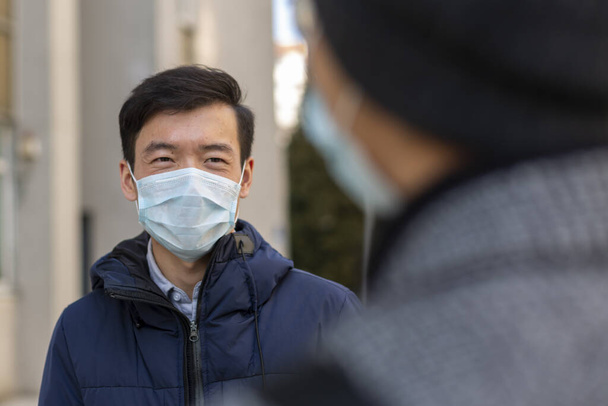 Zwei asiatische junge Männer in medizinischen Schutzmasken gegen das covid-2019-Lächeln, Gespräche - Foto, Bild