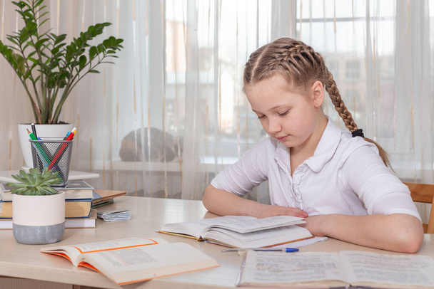 Schoolgirl studying at home. Young girl reading book at the table. Distance education, home education. Self isolation concept - Image - Foto, Bild