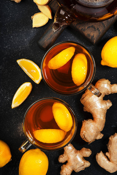 Healing black herbal tea with ginger, honey, lemon and sage. Immune booster drink in glass cup on black kitchen table background with copy space. Top view - Foto, imagen
