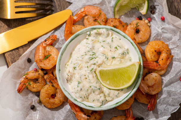 top view of fried shrimps on parchment paper with sauce and lime near cutlery - Foto, Imagen