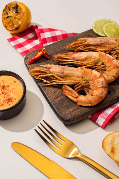 fried shrimps on wooden board on plaid napkin with sauce and lime near golden cutlery on white background - Photo, Image
