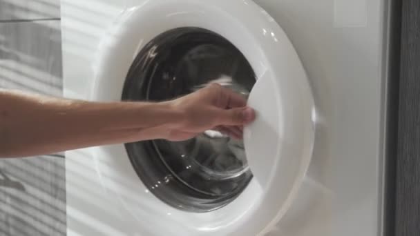 Το αντρικό χέρι βάζει γκρι ρούχα στο πλυντήριο. Φόρτωση πλυντηρίου. Φόρτωσε ρούχα στο πλυντήριο. Φορτώστε ρούχα πλυντήριο ρούχων. Προετοιμασία πλυσίματος ρούχων - Πλάνα, βίντεο