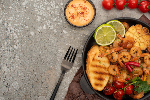 top view of fried shrimps with sauce, fork, grilled toasts, vegetables and lime on grey concrete background - Foto, Imagem