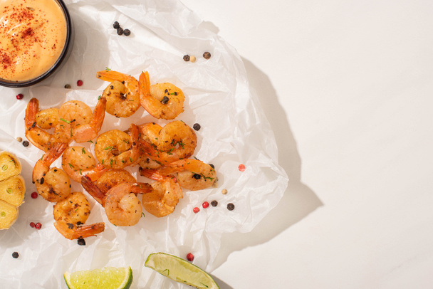 top view of fried shrimps on parchment paper with pepper, sauce and lime on white background - Photo, Image