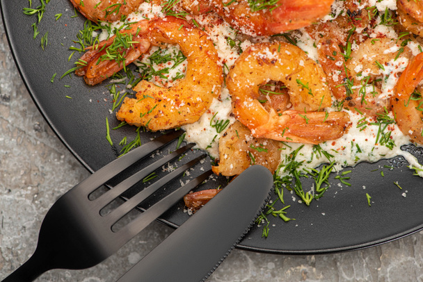 close up view of fried shrimps in sauce with dill in black plate on grey concrete background with cutlery - Photo, Image