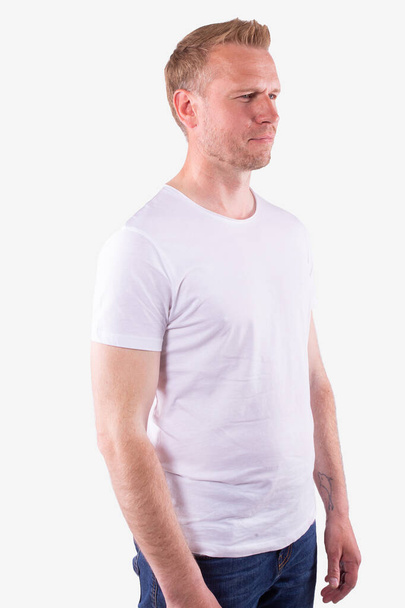 Caucasian man in casual white t-shirt stands half-sides and looks straight ahead - Fotó, kép