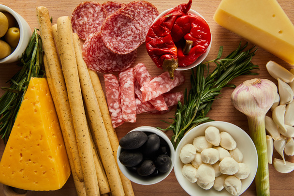 Bovenaanzicht van broodstokjes, salami plakjes, kaas en antipasto ingrediënten op houten ondergrond - Foto, afbeelding