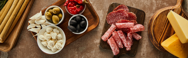 Top view of cheese, salami slices and antipasto ingredients on boards on brown background, panoramic shot - Foto, Imagem