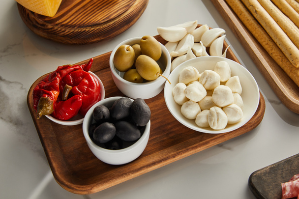 High angle view of boards with breadsticks, garlic and bowls with olives, mozzarella and marinated chili peppers on white - Zdjęcie, obraz