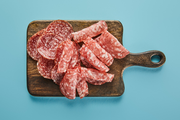Top view of salami slices on board on blue background - Photo, Image